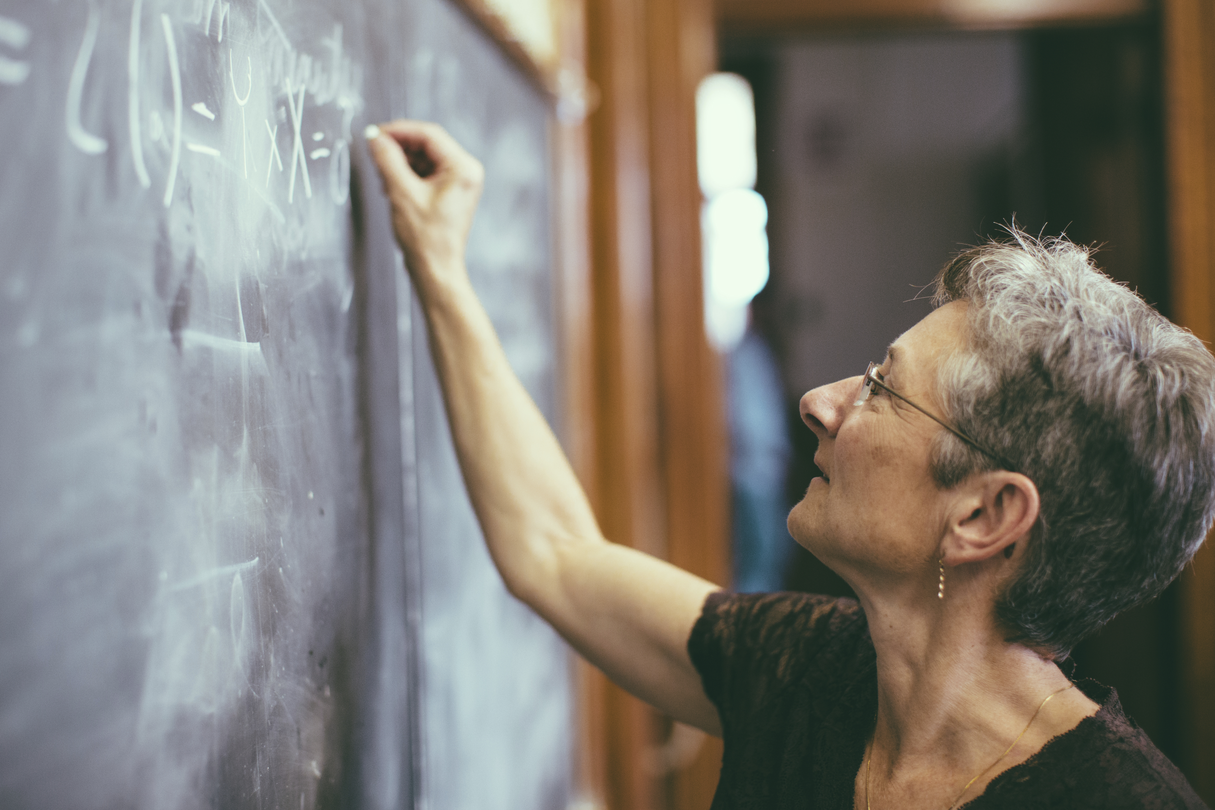 Mathemathics professor at chalkboard writing formula